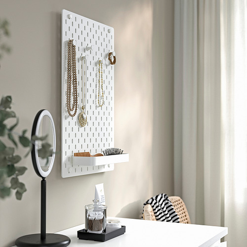 Tablero perforado SKÅDIS blanco de pared con joyas y accesorios, espejo y bandeja sobre un escritorio. Visualización y almacenamiento organizados.