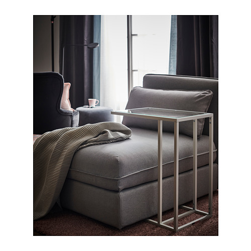Sala de estar moderna con silla reclinable de tela gris, mesa pequeña con tapa de vidrio y manta a rayas.