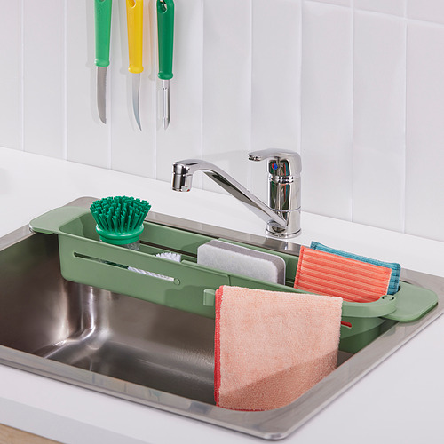 Fregadero de acero inoxidable con organizador SKOLÄST verde que sostiene el cepillo, las esponjas y los paños cerca del grifo cromado.