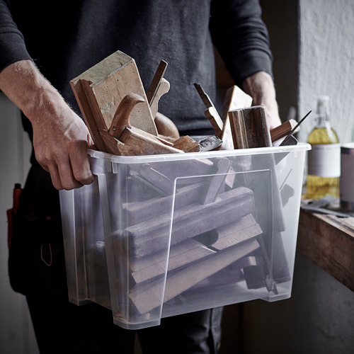 Una persona sostiene un contenedor de plástico transparente lleno de herramientas de madera, listo para organizar y almacenar.