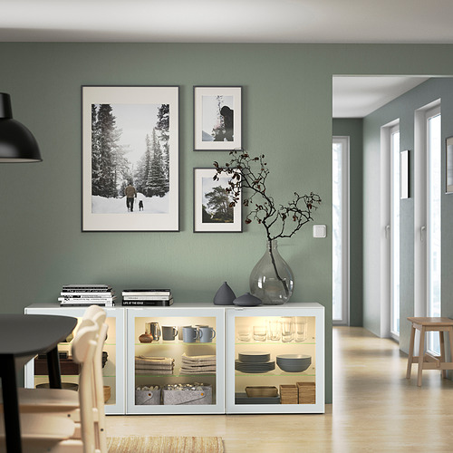 Modern dining room with sage green walls, BESTÅ sideboard with dishes & decor, three framed photos.
