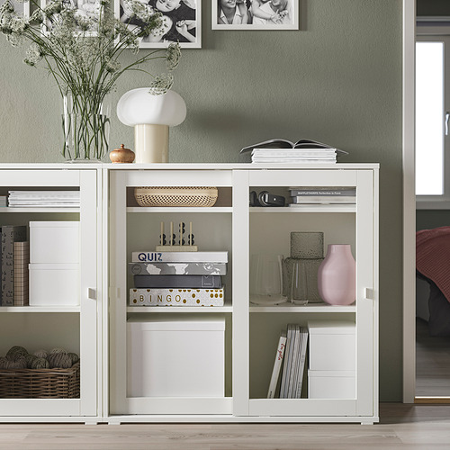 Moderno gabinete con puerta de vidrio blanco, más pequeño que los muebles circundantes, decorado con jarrones, libros y decoración.