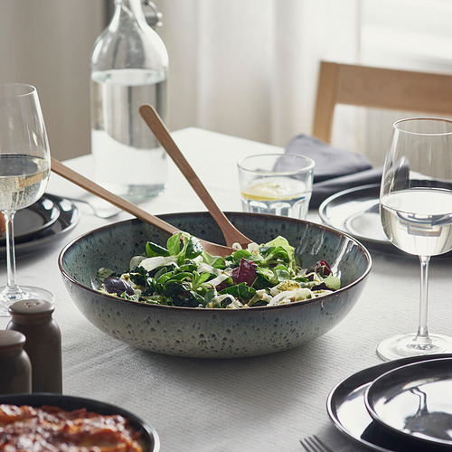 Una mesa rústica con ensalada, pinzas, vasos, cubiertos y una botella.