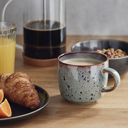 Mesa de madera con productos para el desayuno: jugo de naranja, croissant, granola y café en una taza GLADELIG.