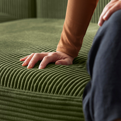 Manos que tocan el sofá JÄTTEBO verde con estampado ondulado. El sofá tiene un diseño moderno y modular con asientos profundos y espacio de almacenamiento.