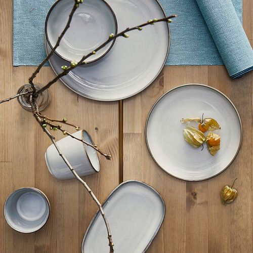 Plato lateral GLADELIG colocado sobre mesa de madera. Forma parte de la serie clásica, más grande que un plato y una taza, que exhibe gres artesanal.