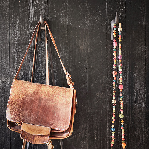 El bolso de cuero marrón cuelga en un gancho junto a decoraciones de cuentas en una pared oscura.