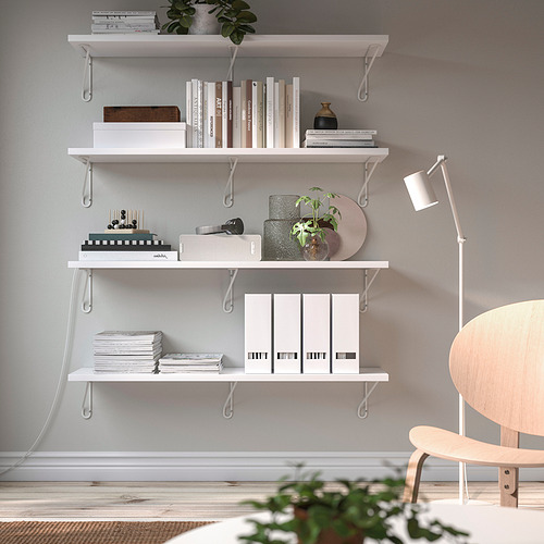 Una moderna zona de estudio con estanterías blancas BERGSHULT que contienen libros, decoración y plantas. Una silla de madera y una lámpara de pie completan el diseño minimalista.