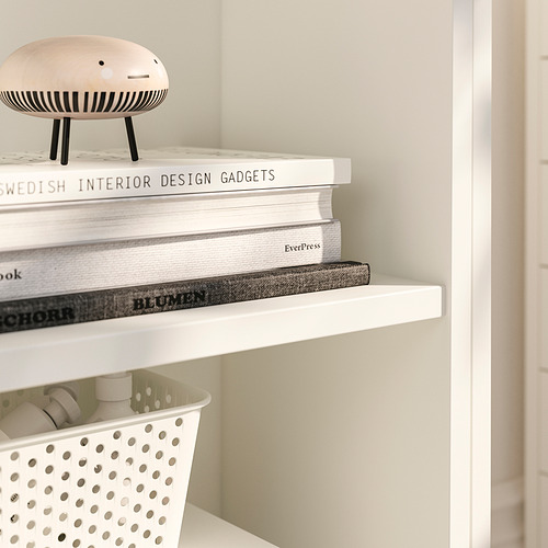 Libros cuidadosamente apilados en un estante blanco de calidad. También hay una figura decorativa y una cesta de almacenamiento.