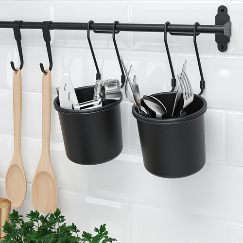 Portautensilios de cocina colgantes negros con cucharas de madera y utensilios de metal en una cocina de azulejos blancos.