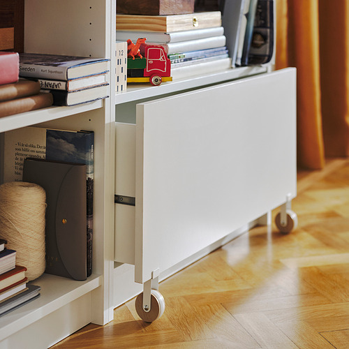 Librería blanca BILLY con cajón sobre suelo de madera, llena de libros y un coche de juguete rojo.