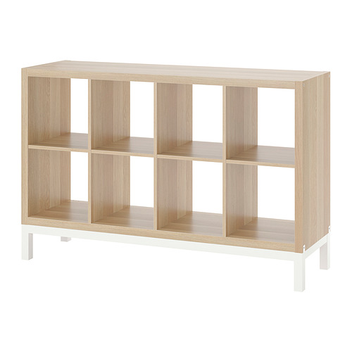 Una estantería KALLAX vacía de madera clara con patas blancas, con varios estantes en forma de cubo.