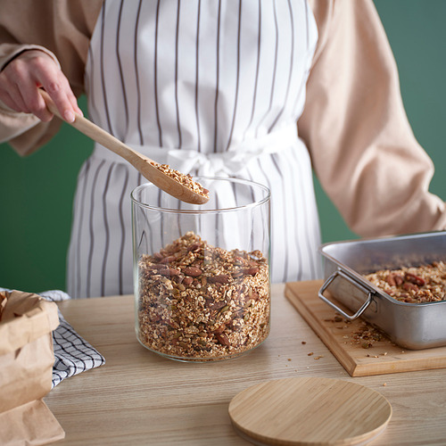 Una persona saca granola de un frasco de vidrio transparente sobre una mesa de madera, ideal para almacenar y acceder fácilmente a alimentos secos.