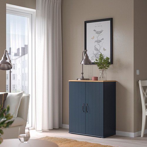 Gabinete SKRUVBY gris en esquina, cerca de la ventana y la silla, rematado con lámpara, vela y jarrón.