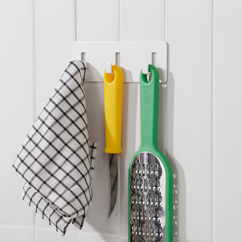 Tres ganchos en una pared blanca sostienen una tela a cuadros, un cuchillo amarillo y un rallador verde. Organiza los utensilios de cocina de manera eficiente.