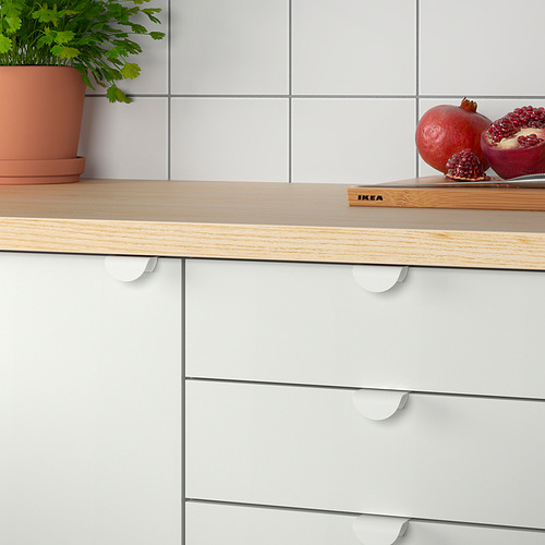 Una moderna encimera de cocina con cajones blancos con tiradores de clip DRAGSMARK, una encimera de madera, granadas y una planta.