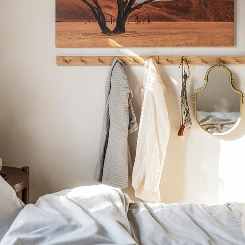 Dormitorio con cama blanca, perchero de roble, toallas grises y blancas, espejo dorado, arte del desierto.