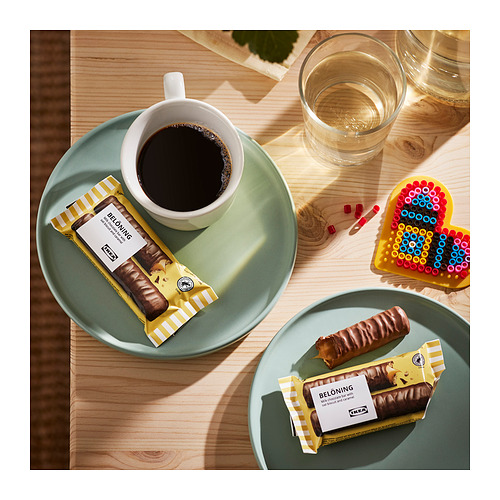 Vista superior de dos platos verdes con barras de chocolate belaning, uno sin envolver, y una taza de café sobre una mesa de madera.
