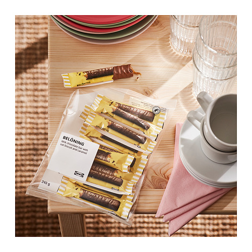 Tabletas de chocolate IKEA BELÖNING, empaquetadas y parcialmente sin envolver, cerca de platos y tazas.