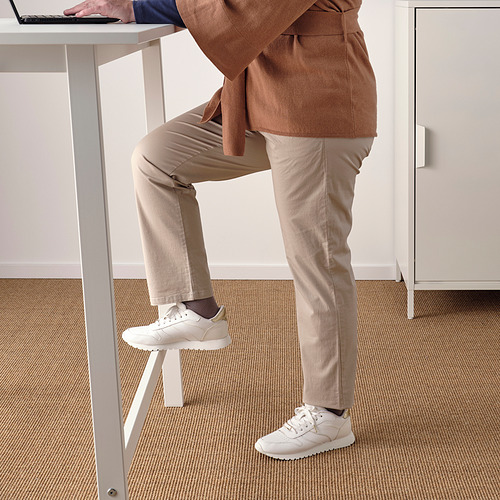 Persona apoyada en una mesa alta con reposapiés, usando computadora portátil.
