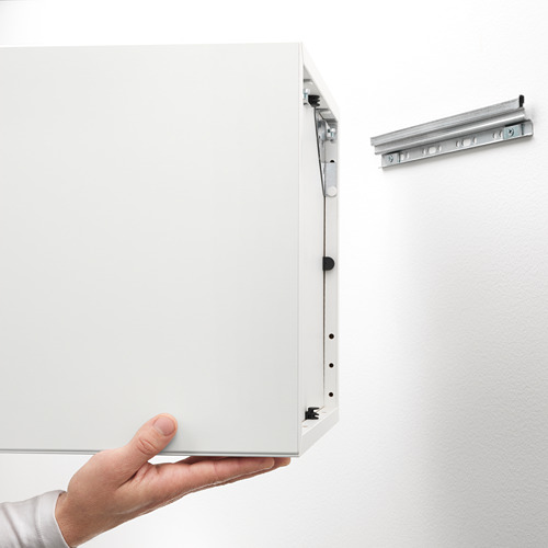 Persona sosteniendo un panel de mueble plano blanco, riel sin empacar y herrajes.