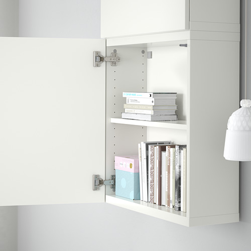 Mueble BESTÅ blanco con bisagras ajustables. Funciones de puerta de cierre suave y apertura a presión. Los estantes contienen libros y organizadores.