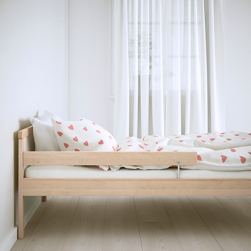 Cama infantil de madera con listones, corazones rosas extendidos, barandilla, cortinas transparentes.