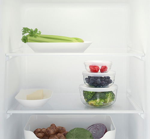 Estantería de nevera con recipientes de vidrio que contienen verduras y sobras, organizados y apilados de manera eficiente.
