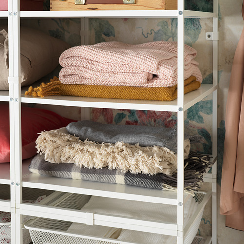 Estante de almacenamiento de metal blanco que contiene mantas y toallas dobladas de color rosa, gris y beige. Cuidadosamente organizado en secciones individuales.