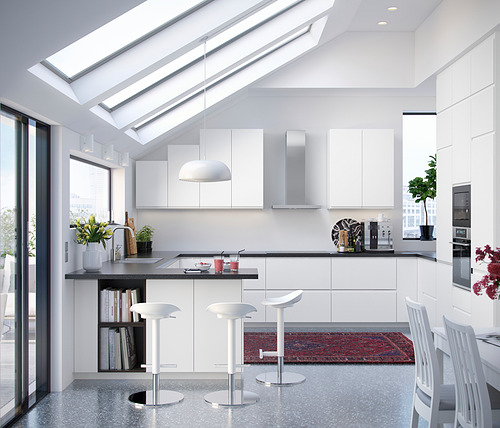 Cocina blanca moderna con gabinetes elegantes, tragaluces, taburetes de bar y plantas.