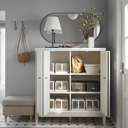 Neat entryway with IDANÄS white cabinet, mirror, lamp, and gray walls. Organized with storage bins, backpacks, flowers, and hooks with bag.