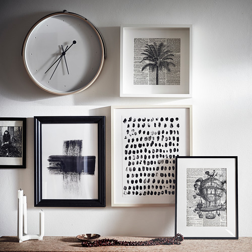 Un reloj blanco silencioso con manecillas negras cuelga sobre una pared con varias obras de arte enmarcadas en blanco y negro.