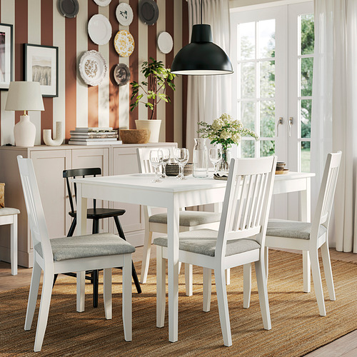Mesa de comedor blanca con 4 sillas grises, extensibles, decoradas con platos, lámpara, libros y jarrones.