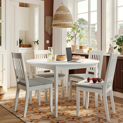 Mesa de comedor redonda blanca con 4 sillas grises, rodeada de plantas.