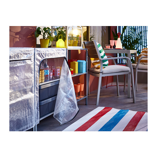 Pequeño invernadero sobre ruedas con plantas en macetas, tazas de colores y silla a rayas.