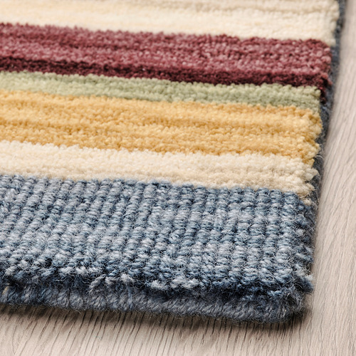 Alfombra de lana hecha a mano a rayas con bandas horizontales de colores; Textura suave y espesa sobre suelo de madera.