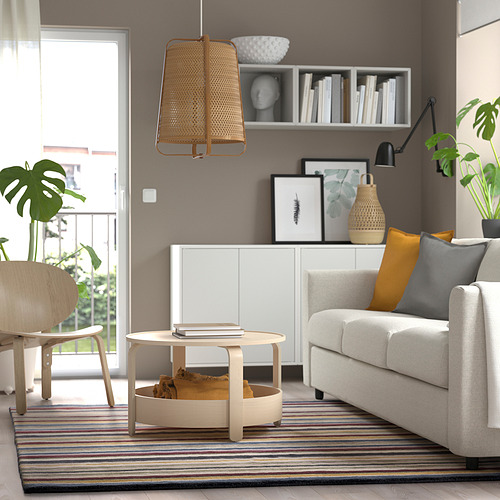 Sala de estar moderna con alfombra de colores, sofá gris, almohadas amarillas, mesa de centro de madera y plantas.