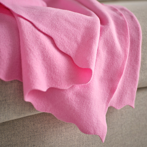 Manta de vellón suave de color rosa brillante sobre una superficie beige, mostrando su textura acogedora y su calidez acogedora.