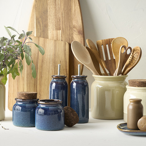 Jarras azules BRUGDHAJ en gres, tapas de corcho, tamaños variados. Con utensilios de madera, tabla de cortar, planta. Diseño rústico.