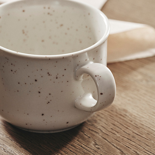 Taza sobre mesa de madera, beige claro con manchas oscuras, diseño moteado de calidad.