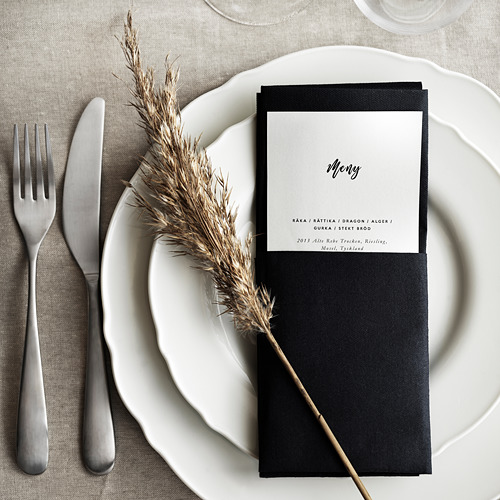 Mesa con servilleta negra, plato blanco, tenedor, cuchillo y planta seca, elegante y sencillo.