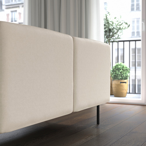 Sofá modular beige, con respaldo alto, cerca de la ventana, sobre suelo de madera.