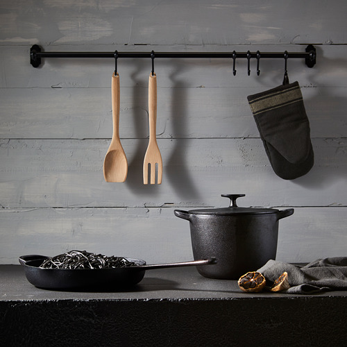 Escena de cocina con ollas, sartenes, utensilios de madera y guante en ganchos de pared. Configuración rústica y organizada.