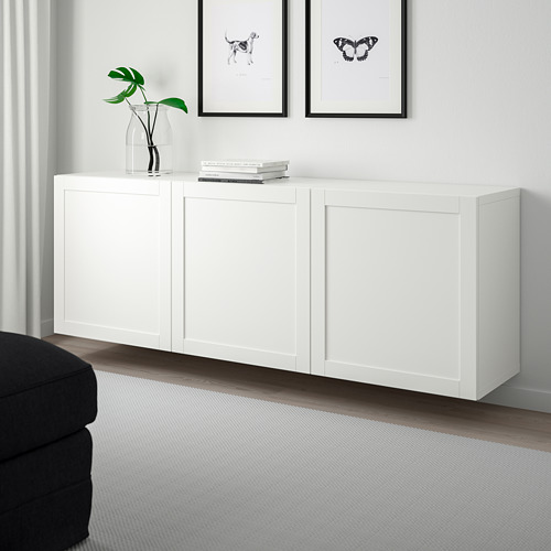 Armario blanco BESTÅ con estantes ajustables, puertas de cierre suave, jarrón de sujeción, libros y cuadros en blanco y negro, sofá gris oscuro, alfombra clara debajo.