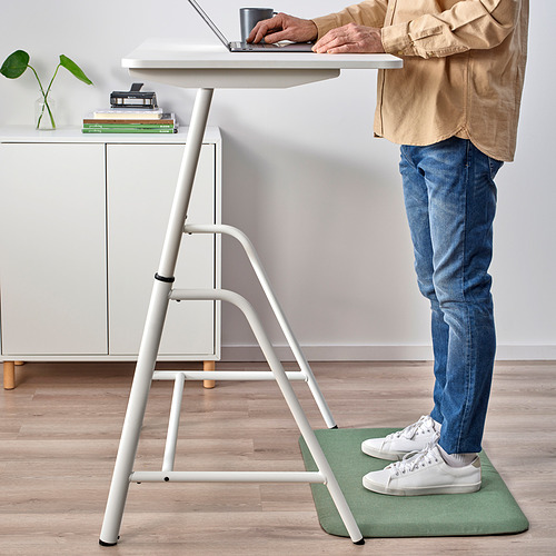 Persona en la estera FREIVID, escribiendo en una computadora portátil en un escritorio blanco con planta, libros, taza.