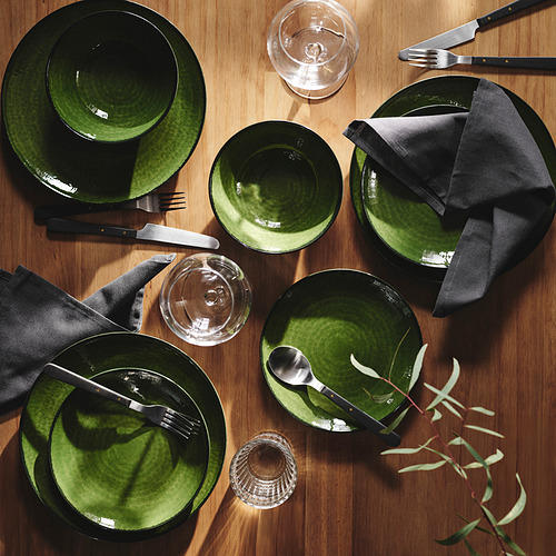 Puesto de gres verde sobre la mesa: platos, cuencos, vasos, cubiertos negros, servilletas dobladas.