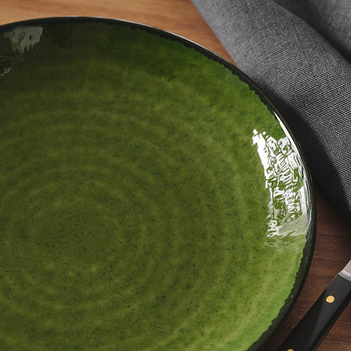 Plato verde alargado sobre la mesa, acabado brillante, centro más profundo, borde más oscuro.