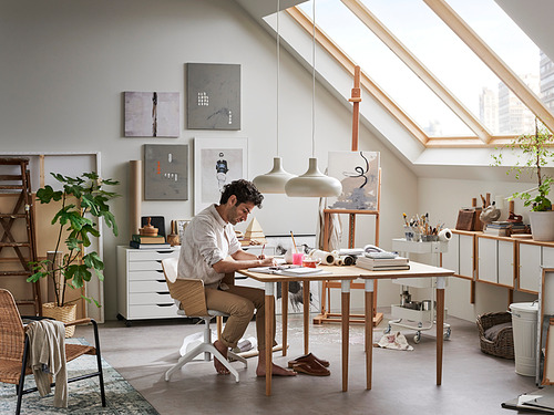 El artista trabaja en un estudio luminoso y moderno con mesa de bambú ANFALLARE, arte en las paredes, plantas y luz natural.