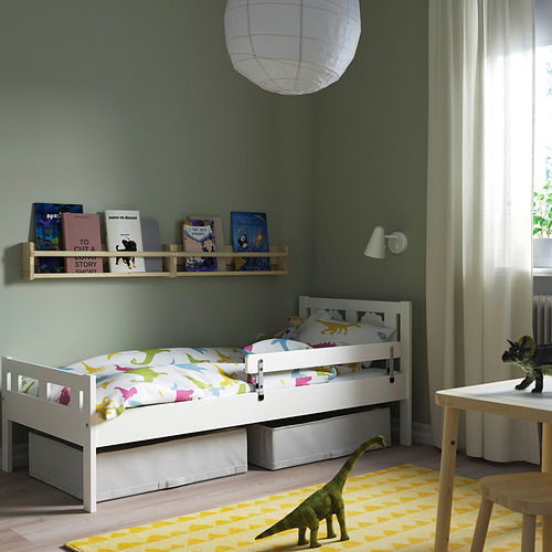 Habitación de niños: cama KRITTER, ropa de cama de dinosaurio, muebles de madera, alfombra amarilla. Estantería, juguetes, cortinas ligeras, lámpara de pared.