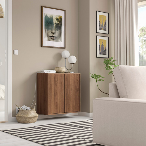 Habitación moderna con mueble EKET de madera, alfombra blanco y negro y sillón gris. El arte y las plantas decoran el espacio.